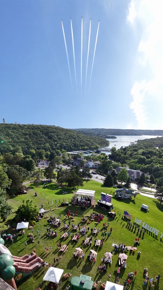 Aerial drone panorama of an outdoor lakeside event in the Branson, Missouri Ozarks with jet contrails overhead